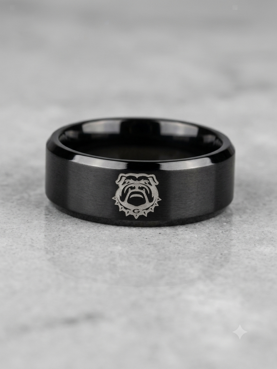 A black metallic band ring with a brushed finish and a silver bulldog emblem in the center, resting on a light gray stone surface.